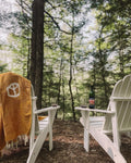 Cozy outdoor scene featuring a Peace Blanket draped over an Adirondack chair, surrounded by nature.