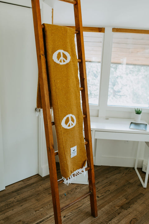 Cozy handwoven Peace Blanket from Trek Light on wooden ladder, made from recycled clothing materials.