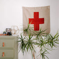 Decorative Positive Vibrations Blankestry with red cross design, made from recycled materials, hanging above a dresser. Trek Light home decor.