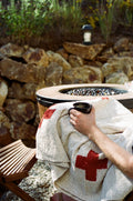 Person holding a cup while wrapped in a Positive Vibrations Blanket next to a fire pit.