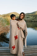 Mother and child wrapped in a Trek Light Positive Vibrations Blanket by the lake, featuring handmade recycled materials and unique design.