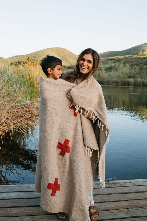 Mother and child wrapped in a Trek Light Positive Vibrations Blanket by the lake, featuring handmade recycled materials and unique design.