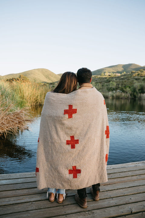 Couple cuddling under a handwoven Positive Vibrations Blanket by Trek Light, nature backdrop, sustainable recycled materials