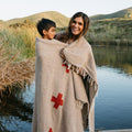 Mother and child wrapped in a Trek Light Positive Vibrations Blanket by the lake, featuring handmade recycled materials and unique design.