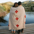 Couple cuddling under a handwoven Positive Vibrations Blanket by Trek Light, nature backdrop, sustainable recycled materials