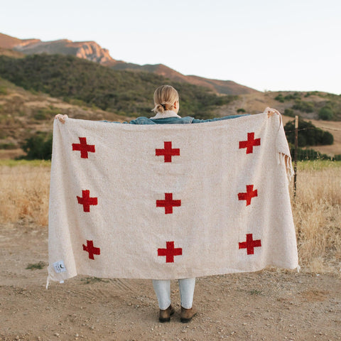 Person holding Trek Light Positive Vibrations Blanket, handwoven with recycled materials, featuring red crosses and a sustainable design.