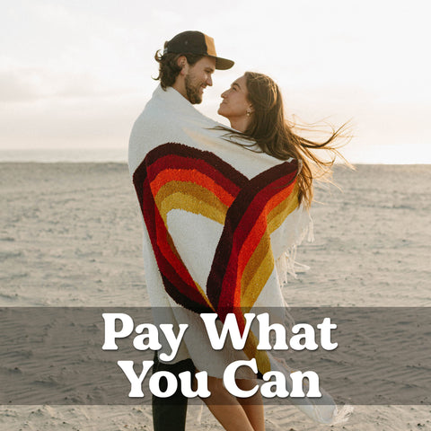 Couple on a beach with a colorful Trek Light blanket, text 'Pay What You Can' overlaid.