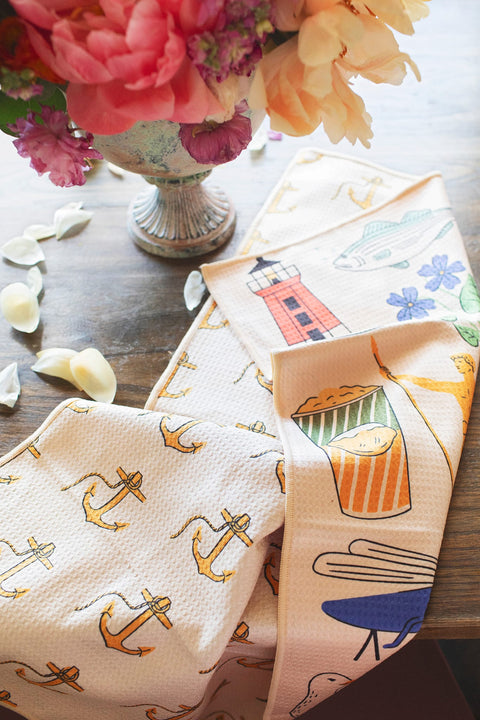 Rhode Island Kitchen & Tea Towel with vibrant anchor, lighthouse, and fish designs on a table.