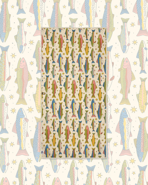 River Trout Wander & Travel Towel in cream with colorful trout and stars, laid over a matching fish pattern.