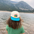 Child wearing the Rock N Roll Kids Hat by a serene lake with mountains in the background.