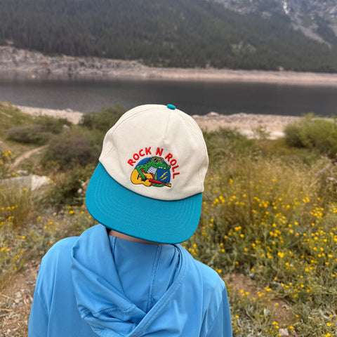 Child wearing a Rock N Roll Kids Hat while enjoying outdoor adventures near a lake.