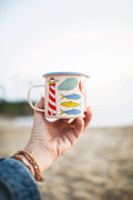 Hand holding a Salty Seas Enamel Mug 16oz with nautical lighthouse and fish design, perfect for camping and cozy mornings.