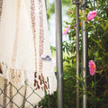 Handwoven Silverton blanket with stripes, made from recycled materials, hanging near pink flowers outdoors.