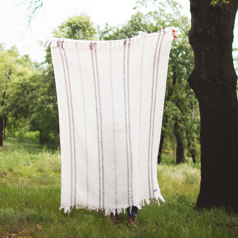 Person holding Silverton Blanket outdoors, showcasing handwoven stripes made from 100% recycled materials, sustainable and unique design.