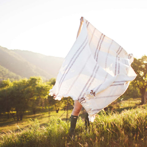 Person holding the Silverton Blanket with geometric stripes outdoors, highlighting its sustainable, handwoven design from recycled materials.