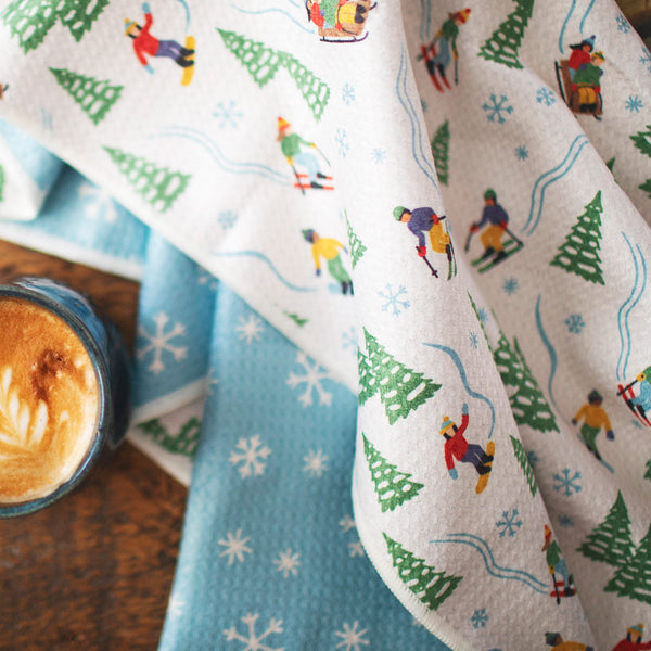 Snow Day Kitchen & Tea Towel with vibrant winter design, eco-friendly, super absorbent Grip-Tex™ fabric, displayed with a cup of coffee.