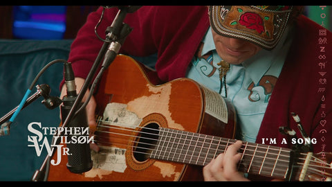 Musician playing acoustic guitar with 'I'm a Song' text overlay on screen.