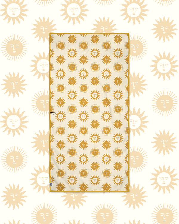 Sunny Wander & Travel Towel in cream with gold sun face print and gold trim, laid flat on a matching sun pattern background.