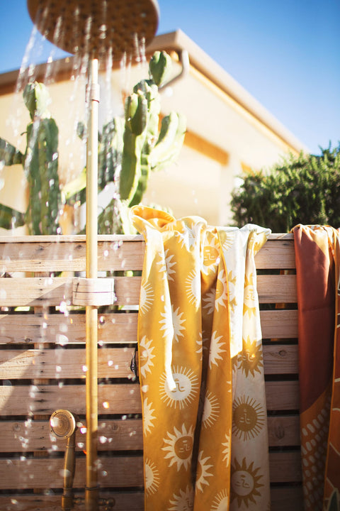 Sunny Wander & Travel Towel hanging near a shower, featuring a vibrant sunshine design.