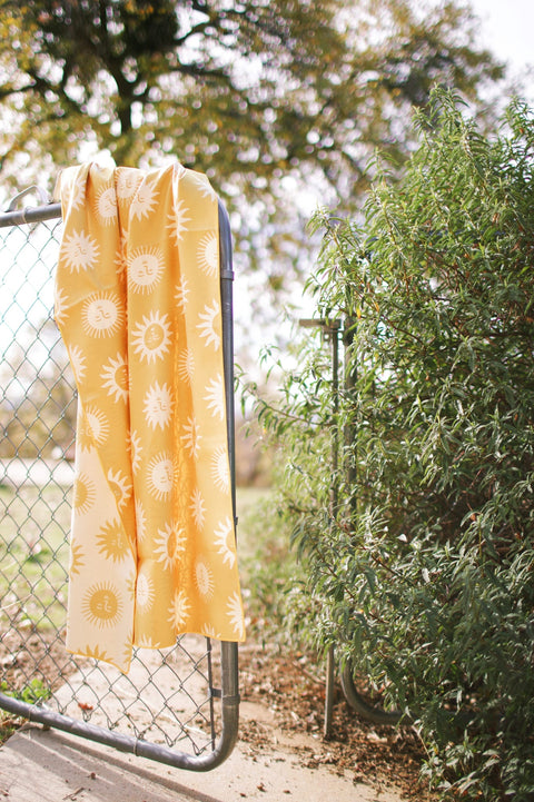 Sunny Wander & Travel Towel hanging on a fence, showcasing its vibrant sunshine design and travel-friendly size.