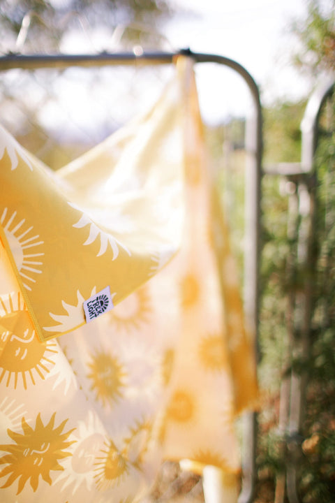 Sunny Wander & Travel Towel showcasing a vibrant sunshine design hanging outdoors.