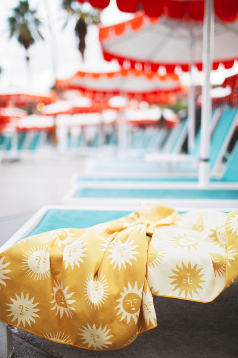 Sunny Wander & Travel Towel with vibrant sunshine design on a lounge chair by the pool.