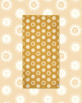 Sunny Wander & Travel Towel in mustard yellow with cream sun face print, laid flat on a peach background of larger suns.