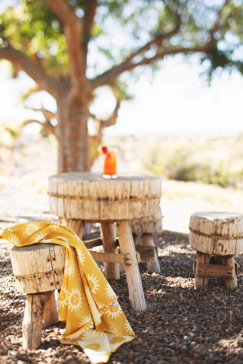 Sunny Wander & Travel Towel draped over a wooden stool in a sunny outdoor setting.