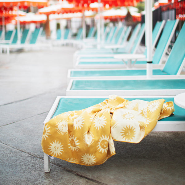 Sunny Wander & Travel Towel on a sun lounger by a pool, featuring quick-dry and sand-resistant properties.