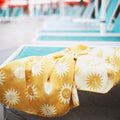 Sunny Wander & Travel Towel on a lounge chair by the pool, featuring a bright sun pattern. Quick-dry and sand-resistant.