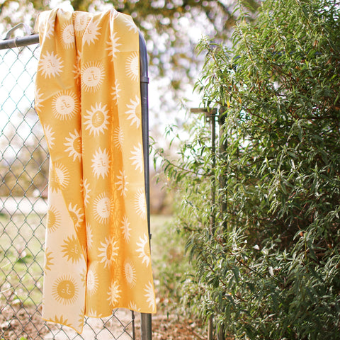 Sunny Wander & Travel Towel hanging on a fence, featuring a yellow sun design, perfect for quick drying and sand-resistant travel.