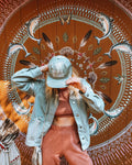 Person wearing a Take Me To The River Hat in front of a colorful mural featuring fish and nature elements.