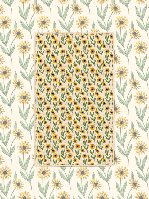 Yellow and green black-eyed Susan pattern towel laid flat over a matching daisy print background
