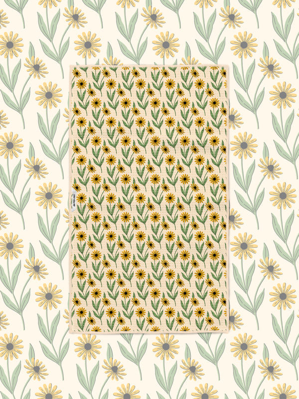Yellow and green black-eyed Susan pattern towel laid flat over a matching daisy print background