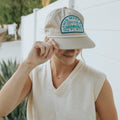 Smiling person wearing a 'This Must Be The Place' beach-themed snapback hat by Trek Light, perfect for sunny adventures.