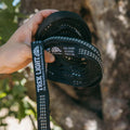 Hand holding Trek Light Go Anywhere Hammock Straps with trees in the background.