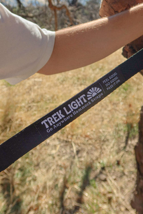 Close up of a black Go Anywhere Pro Hammock Straps webbing strap with the Trek Light logo held by a tree
