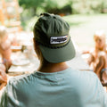 Trout Hat worn by a person outdoors, showcasing its adjustable design and unique trout logo in a casual setting.