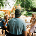 A person wearing a Trout Hat enjoying a meal outdoors with children in a sunny setting.