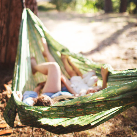 Two people relaxing in a Double Hammock & Pro Hanging Straps (River Trout Print) under a tree.