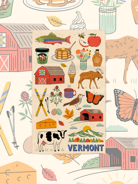 Vermont icon kitchen towel styled over a matching illustrated backdrop of barns, butterflies and fall leaves