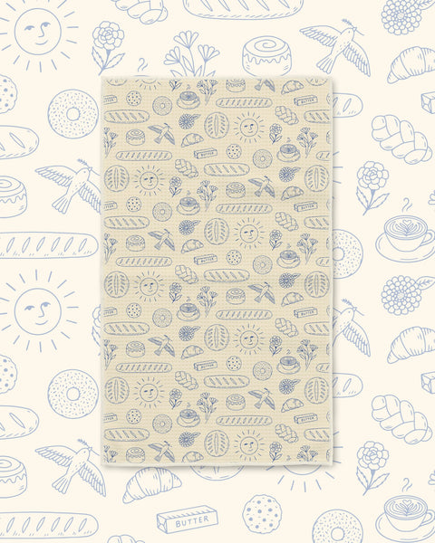 Wake & Bakery Kitchen & Tea Towel with blue line-drawn breads, pastries and suns on a tan background