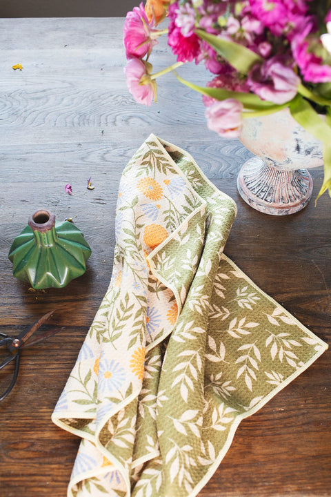 Wavy Flowers Kitchen & Tea Towel displayed on a wooden table with flowers and a vase.