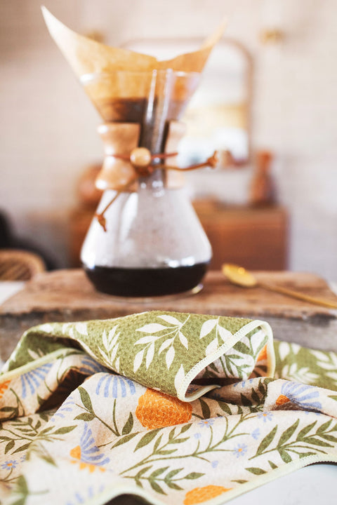 Wavy Flowers Kitchen & Tea Towel on a kitchen counter with coffee maker in the background.