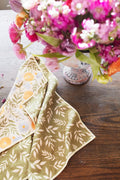 Wavy Flowers Kitchen & Tea Towel on a wooden table with a colorful flower arrangement.
