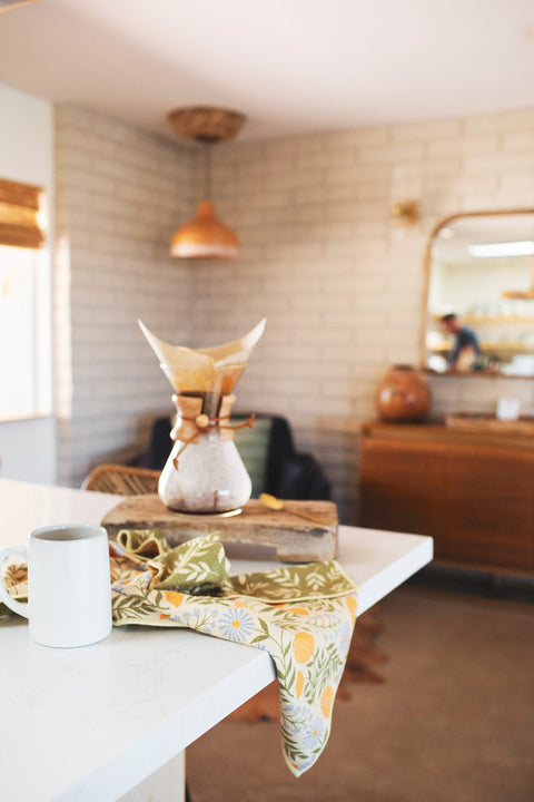 Wavy Flowers Kitchen & Tea Towel on a table with a mug, showcasing vibrant double-sided designs and eco-friendly materials.