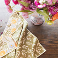 Wavy Flowers Kitchen & Tea Towel on wooden table beside a vase of colorful flowers.