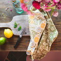 Wavy Flowers Kitchen & Tea Towel draped over a wooden board with lemons, limes, and flowers in a vase.