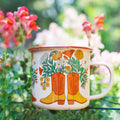 Western Bloom Enamel Mug 16oz with cowboy boot and flower design in a garden setting - Trek Light happiness with every sip.