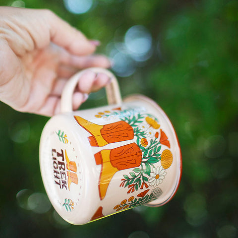 Hand holding Trek Light Western Bloom Enamel Mug 16oz with colorful floral design, perfect for outdoor adventures and happiness.